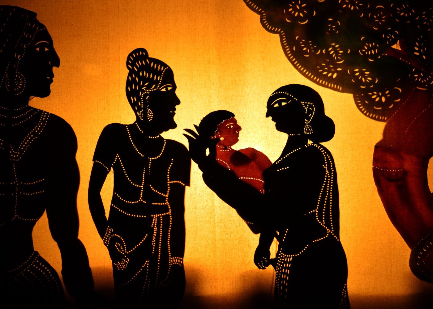 Illuminated leather shadow puppets performing a scene behind a screen